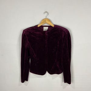 以下が含まれることがあります： ボタン留めと長袖のボルドーベルベットのブレザー。ラベルには「Norma Kamali」と記載されています。