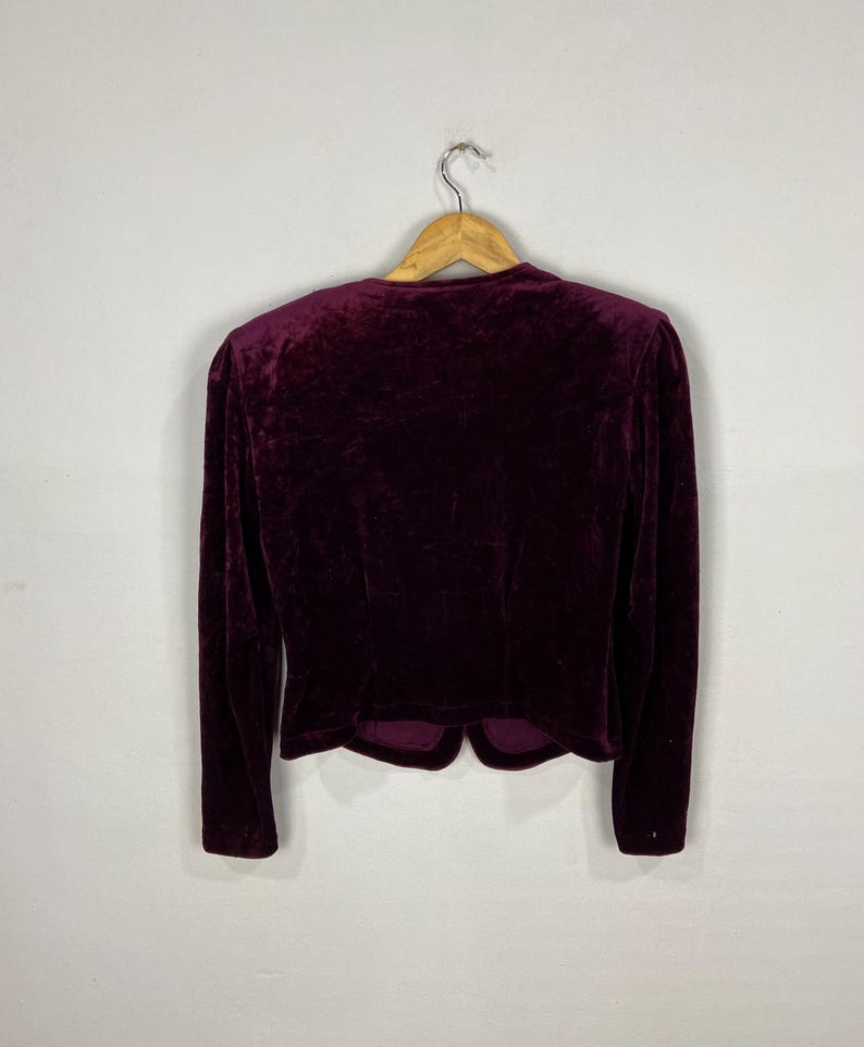 以下が含まれることがあります： 長袖でぴったりとしたシルエットの、濃い赤紫色のベルベットのブレザー。Vネックで、丈が短くなっています。