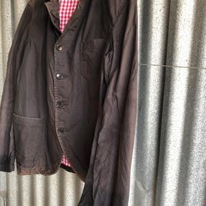 May include: A dark brown blazer with a red and white checkered lining. The blazer has a classic design with a notched lapel, three buttons, and two front pockets. The sleeves are long and the fabric appears to be a lightweight cotton or linen blend.