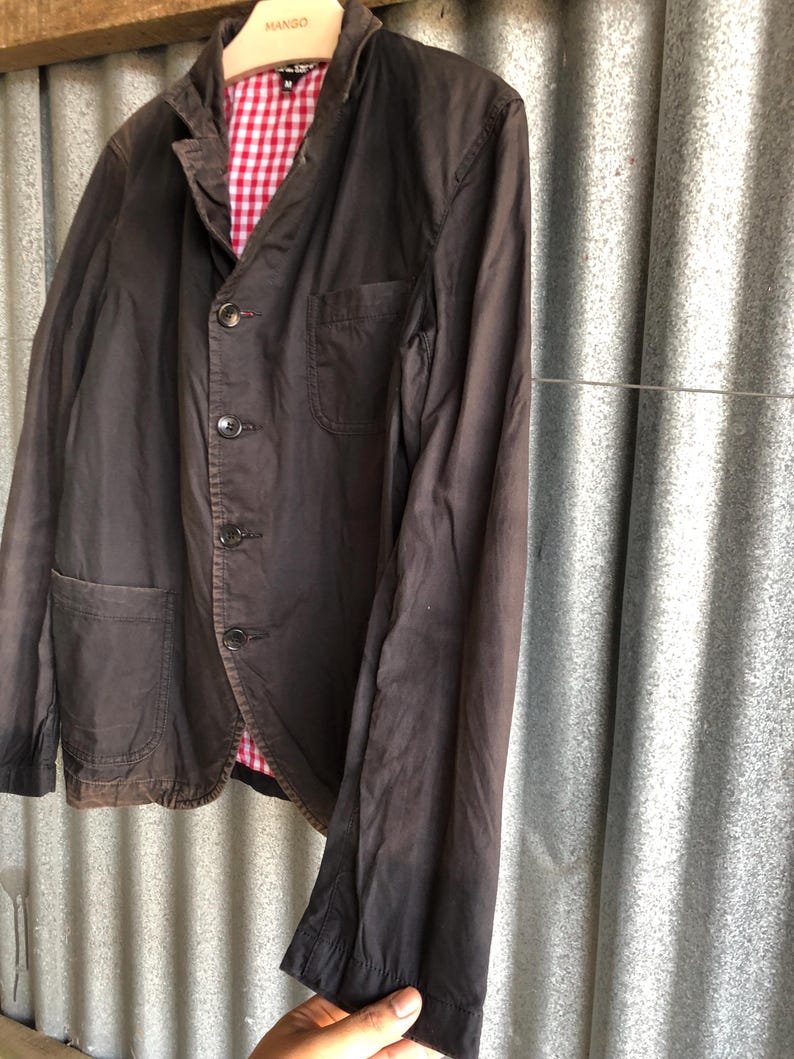 May include: A dark brown blazer with a red and white checkered lining. The blazer has a classic design with a notched lapel, three buttons, and two front pockets. The sleeves are long and the fabric appears to be a lightweight cotton or linen blend.