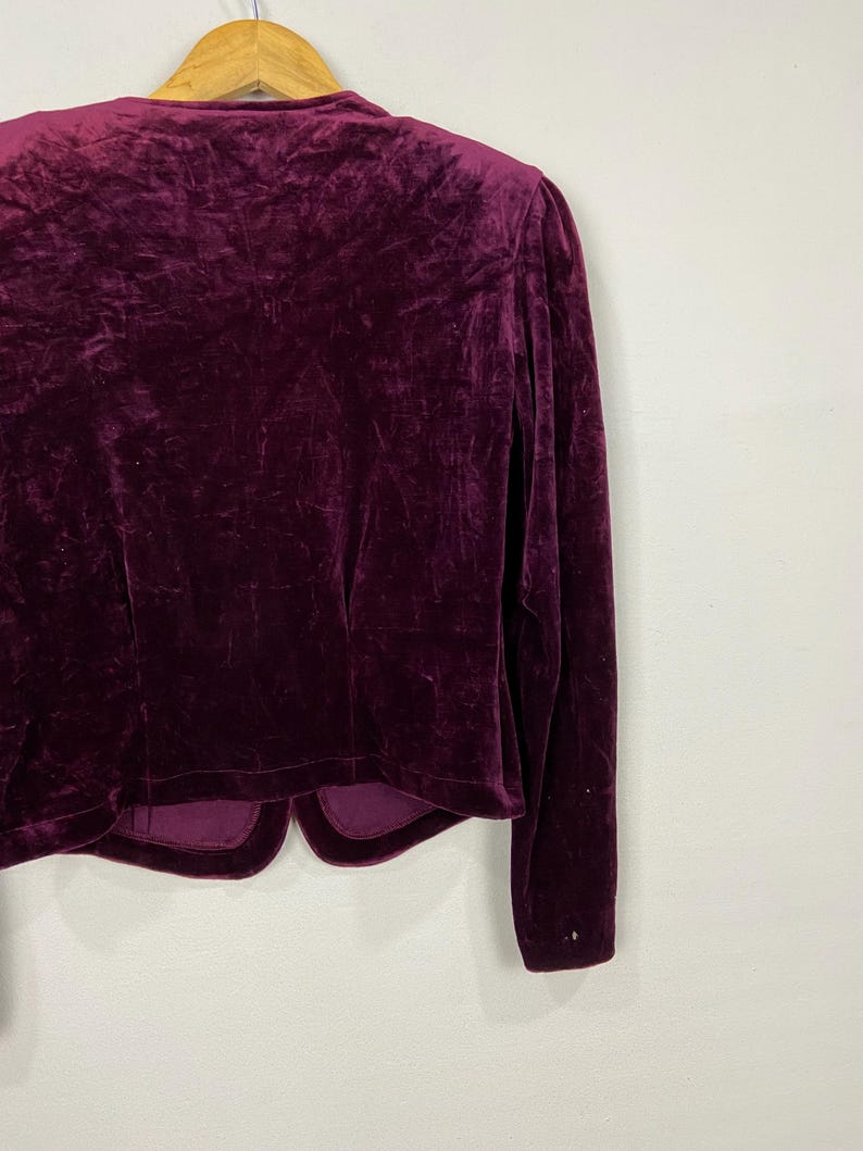 以下が含まれることがあります： 長袖でVネックの濃いパープルのベルベットのブレザー。ブレザーは丈が短く、やや体にフィットしたシルエットです。