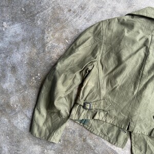 May include: Olive green jacket with a collar and a belt detail at the waist. The jacket has a classic design with a tailored fit. The fabric appears to be a durable material, suitable for various weather conditions.