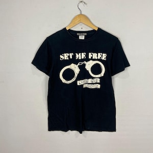 May include: Black t-shirt with a white graphic of handcuffs and the text "Set Me Free" and "Caged Bird Liberty".
