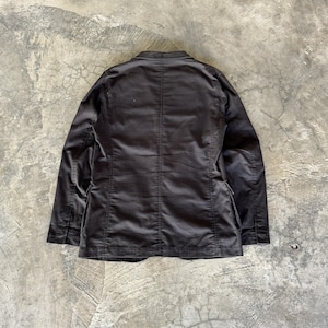 May include: A solid black blazer featuring a structured collar, long sleeves, and a central vertical seam running down the back. The garment is constructed with visible stitching along the shoulders and side panels, showcasing a clean, tailored design.