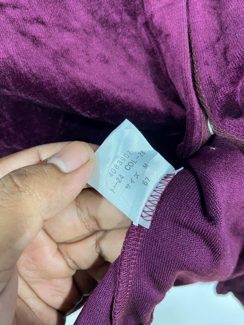 以下が含まれることがあります： 「4089307 1~24 COL~28 サイズ M 67」と黒文字で書かれた白いタグ。タグはワインレッドの生地に付けられています。