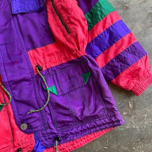 May include: A vintage colour-blocked jacket in purple, pink, and green. The jacket features multiple pockets, a zip-up front, and drawstrings. The sleeves have a striped design, and the jacket has a retro aesthetic.