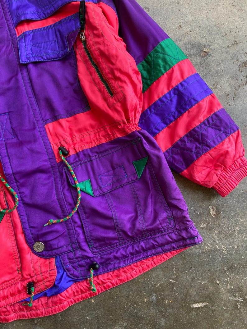 May include: A vintage colour-blocked jacket in purple, pink, and green. The jacket features multiple pockets, a zip-up front, and drawstrings. The sleeves have a striped design, and the jacket has a retro aesthetic.