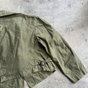 May include: Olive green jacket with a notched collar, shoulder seams, and a belt detail at the waist. The jacket has a classic design with a button closure and a tailored fit. The fabric appears to be a durable cotton or blend, suitable for various weather conditions.