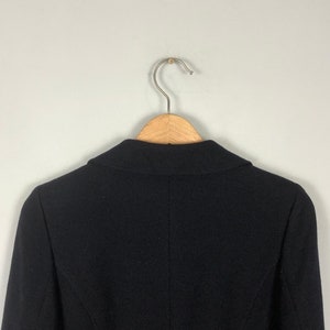 May include: A black blazer hanging on a wooden hanger. The blazer has a classic design with a notched collar and long sleeves.