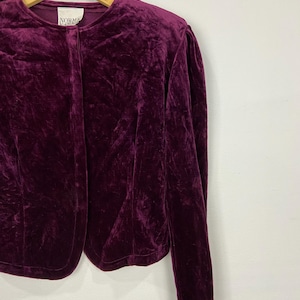 以下が含まれることがあります： ボタン留めと長袖の濃い紫色のベルベットのブレザー。ラベルには「Norma Kamali」と書いてあります。