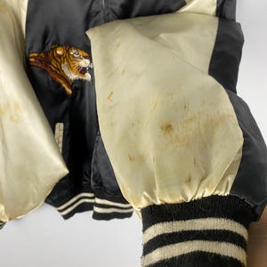 Puede incluir: Chaqueta bomber de sat&eacute;n negro con mangas y detalles en crema. Presenta un tigre bordado en la parte delantera. Los pu&ntilde;os son negros con rayas crema. La chaqueta tiene cierre de cremallera.