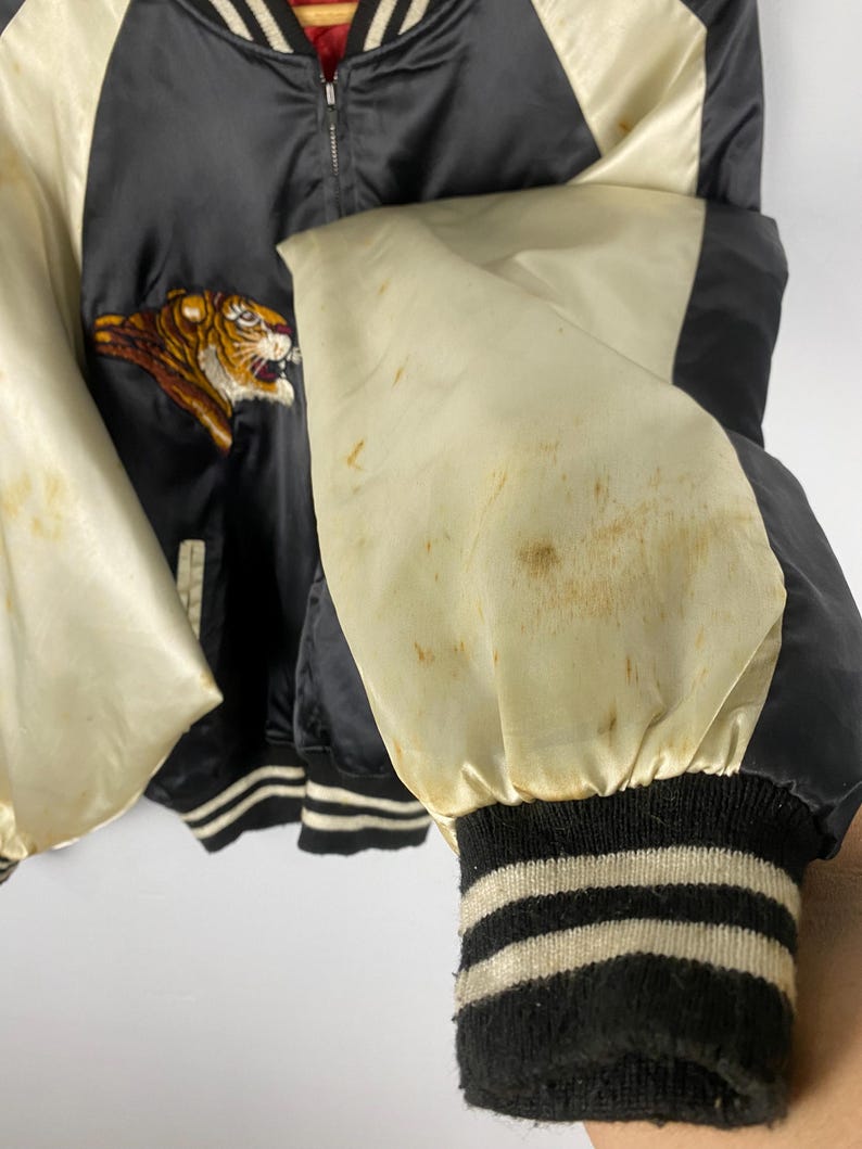 Puede incluir: Chaqueta bomber de sat&eacute;n negro con mangas y detalles en crema. Presenta un tigre bordado en la parte delantera. Los pu&ntilde;os son negros con rayas crema. La chaqueta tiene cierre de cremallera.