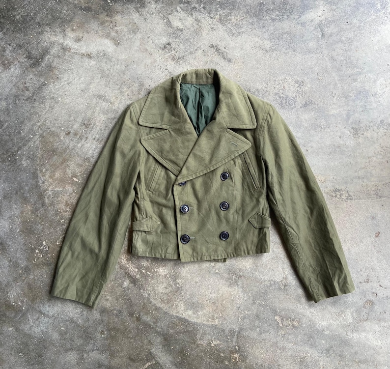 May include: An olive green double-breasted jacket with black buttons. The jacket has a notched collar and two front pockets. The interior lining is a darker green. The jacket is a cropped style.