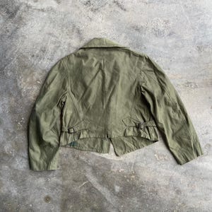 May include: Olive green jacket with a collar and two small buckles on the back. The jacket has a tailored fit and a classic design. The fabric appears to be a lightweight material, suitable for layering.