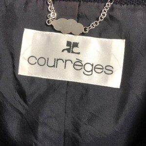 May include: A white label with black text that reads "Courr&egrave;ges" with a stylized "C" logo above the text. The label is attached to a black fabric with a silver chain.