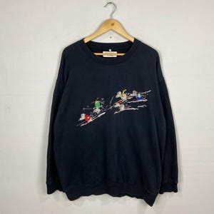 May include: Black long-sleeve sweatshirt with a crew neck and embroidered image of skiers on a snowy mountain. The text "Merry & Bright" is embroidered on the tag.