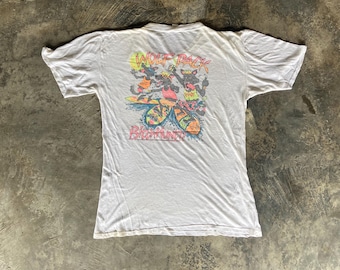 May include: A white short-sleeved t-shirt featuring a colourful graphic on the back. The design depicts three anthropomorphic wolves surfing, with the text WOLF PACK above and BitchHunter below in a stylised, vibrant font with yellow and pink accents.