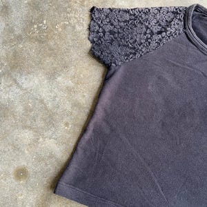 Pu&ograve; includere: Una maglietta grigio scuro con girocollo e maniche corte. La manica destra &egrave; realizzata in pizzo grigio scuro, che aggiunge consistenza e dettagli al design. La maglietta &egrave; realizzata in un materiale morbido.