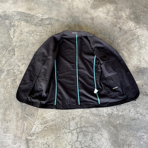 May include: A black blazer shown from the inside, featuring a solid black lining with bright turquoise piping along the seams. The garment includes an interior chest pocket on the right side and a small white care label attached to the lower seam.