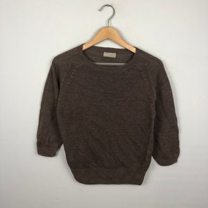 May include: A brown knitted sweater with a round neckline and long sleeves. The sweater is hanging on a wooden hanger.