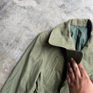 May include: Olive green jacket with a notched collar and a zippered chest pocket. The jacket has a green lining and a classic design. The fabric appears to be a durable material, suitable for various weather conditions.