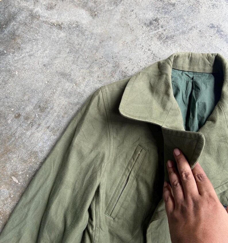 May include: Olive green jacket with a notched collar and a zippered chest pocket. The jacket has a green lining and a classic design. The fabric appears to be a durable material, suitable for various weather conditions.