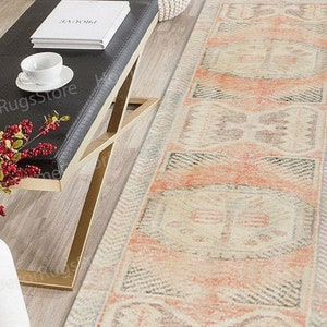 May include: A long, rectangular rug with a cream background and a repeating pattern of peach, grey, and white geometric shapes. The rug has a faded, vintage look.