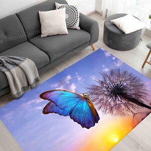 May include: A blue butterfly with purple accents sits on a dandelion seed head against a purple and orange sunset sky. The butterfly is in focus, while the dandelion and sky are blurred.