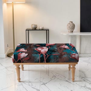May include: A rectangular ottoman with a floral pattern featuring pink magnolia blossoms on a teal and brown background. The ottoman has light-colored wooden legs and a cushioned top, suitable for a living room or bedroom.