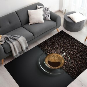 May include: A black and brown area rug with a design of coffee beans and a glass cup of coffee with foam on top. The rug is on a light wood floor in a living room setting.