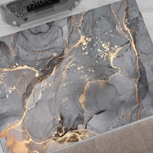 Könnte beinhalten: Abstrakter Teppich mit einem grauen und goldenen Marmormuster. Der Teppich zeigt wirbelnde Muster in Grau und Schwarz mit goldenen Akzenten.