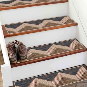 Op de afbeelding: Rechthoekige traptreden met een donkerblauwe en bruine textuurachtergrond en een herhalend wit en beige chevronpatroon. De treden hebben afgewerkte randen en liggen op houten traptreden, met een paar bruine leren laarzen ernaast.