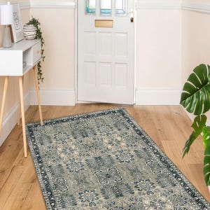 May include: A rectangular rug with a floral design in grey and navy blue tones. The rug, with a dark blue border, is laid on a wooden floor in a hallway. The pattern includes stylized flowers and leaves, creating a classic look.