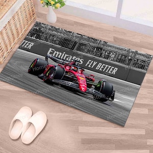 Op de afbeelding: Een zwart-witfoto van een rode raceauto op een circuit. De auto is in beweging en de woorden "Emirates Fly Better" zijn zichtbaar op de zijkant van de auto.