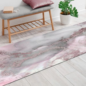 Puede incluir: Una alfombra rectangular larga con un diseño tipo mármol en tonos grises, rosas y oro rosa. La alfombra presenta un patrón fluido con acentos de purpurina, creando una estética lujosa y elegante. Adecuada para la decoración del hogar.