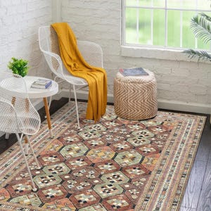 May include: A rectangular area rug with a geometric pattern in shades of brown, orange, green, and beige. The rug has a border with a repeating design. The rug is placed on a dark wood floor.