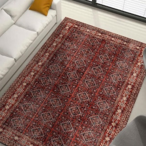Könnte beinhalten: Ein rechteckiger Teppich mit rotem und schwarzem Muster. Der Teppich hat ein kompliziertes Design mit geometrischen und floralen Motiven. Der Rand hat ein cremefarbenes Muster. Der Teppich liegt auf einem hellen Boden.