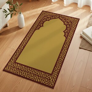 May include: A rectangular prayer rug with a golden center and a decorative burgundy border featuring an arch design. The rug is placed on a wooden floor, suggesting a home setting.