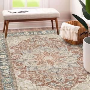 Pode incluir: Um tapete retangular com um design desgastado de inspiração vintage. O tapete apresenta um padrão de medalhão central em tons de ferrugem, creme e azul. A borda é azul escuro com motivos florais. O tapete está numa sala bem iluminada.