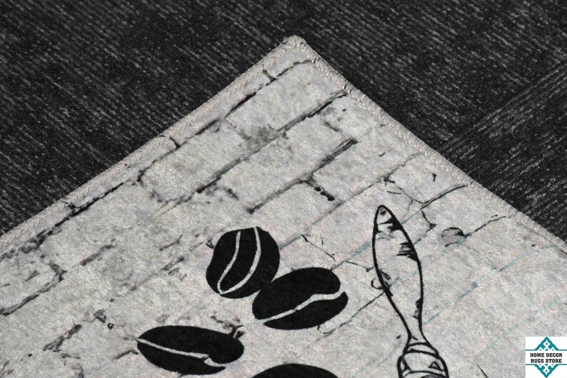 May include: A close-up of a gray and white kitchen rug with a brick pattern. The rug features a black and white illustration of coffee beans and a spoon.