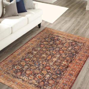 May include: An ornate rectangular area rug with a dark blue background and a detailed floral pattern in shades of orange, red, and blue. The rug has a wide border in a lighter orange hue, adding a contrasting frame to the design. The rug is placed on a wooden floor.