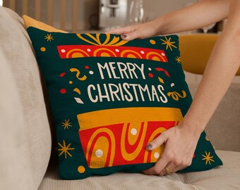 May include: A decorative Christmas pillow with a dark teal background. The pillow features a gift box design in red and yellow, with the words "MERRY CHRISTMAS" in white. Gold star and confetti accents complete the festive look.