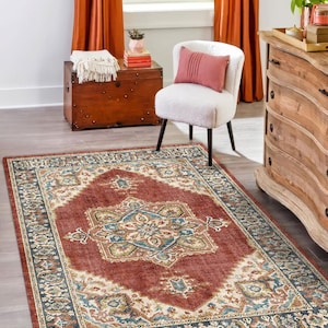 May include: A rectangular area rug with an ornate, traditional design. The rug features a central medallion in shades of red, blue, and beige, surrounded by a detailed border. The rug is placed on a wooden floor, with a chair and chest in the background.