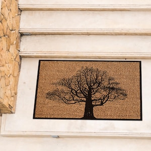 Puede incluir: Una alfombra de coco marrón con una silueta negra de un árbol en el centro.