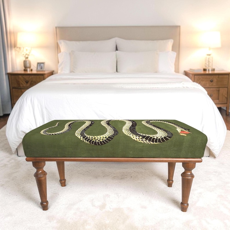 May include: A rectangular bench with a dark olive green upholstered top featuring a long, winding snake graphic in black and yellow with a red tongue. The bench is supported by four turned wooden legs in a medium brown finish.