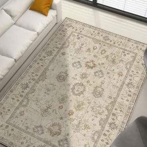 May include: A rectangular area rug with an ornate floral pattern in beige, gray, and muted green tones. The rug has a detailed border and is placed on a light-colored floor. The rug is in a living room setting.