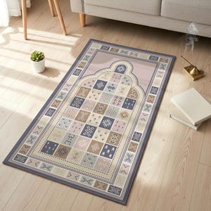 Könnte beinhalten: Rechteckiger Gebetsteppich mit geometrischem Muster in Blau-, Beige- und Rosatönen. Der Teppich hat ein zentrales Bogendesign und einen Rand mit sich wiederholenden geometrischen Motiven. Der Teppich liegt auf einem hellen Holzboden.