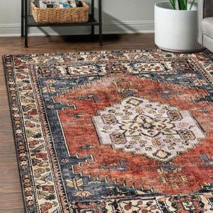 May include: A rectangular rug with a distressed, vintage design. The rug has a central medallion in cream and beige, surrounded by a rust-coloured field and navy blue borders. The rug is placed on a wooden floor.