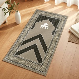 May include: A rectangular prayer mat with a mosque design. The mat has a grey background with black and grey geometric patterns and a decorative border. It is placed on a wooden floor.