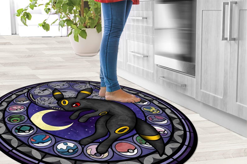 May include: A round, purple and black rug with a stained glass design featuring a black and yellow Pokemon character. The character is standing on a crescent moon with a starry background. The rug is surrounded by a black border.